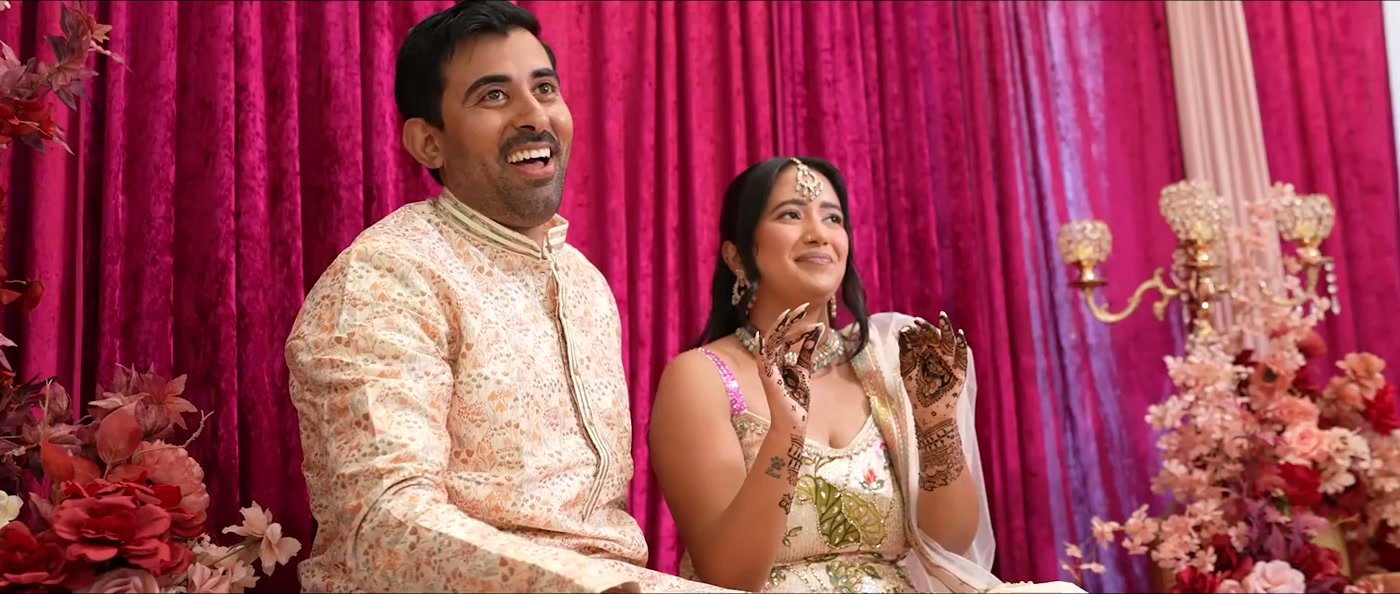 The couple laughing during the ceremony, deep pink drapes behind them
