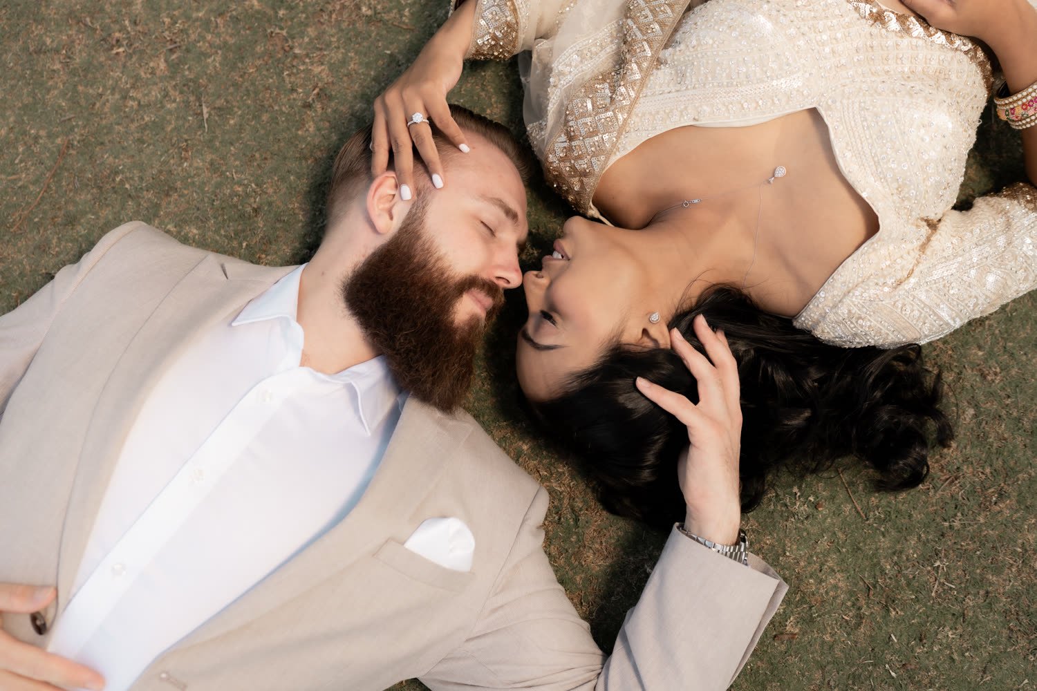 A couple lying on the grass together after their ceremony, foreheads almost touching